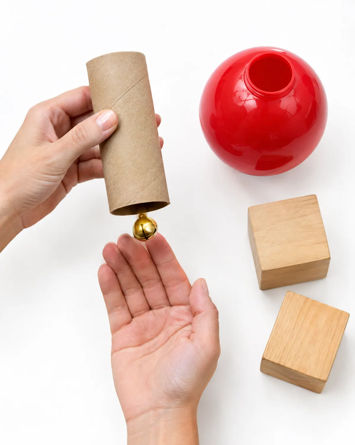 Choke tube test for a Christmas sensory bin: a toilet paper tube on a table beside a small jingle bell that fits through it and a large plastic ornament that does not