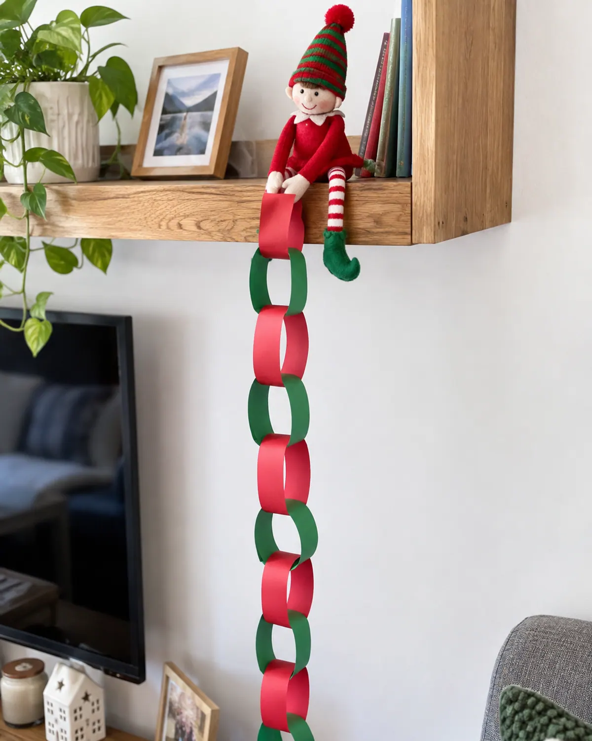 A red and green paper chain countdown hanging from a shelf with a felt elf doll holding the bottom link