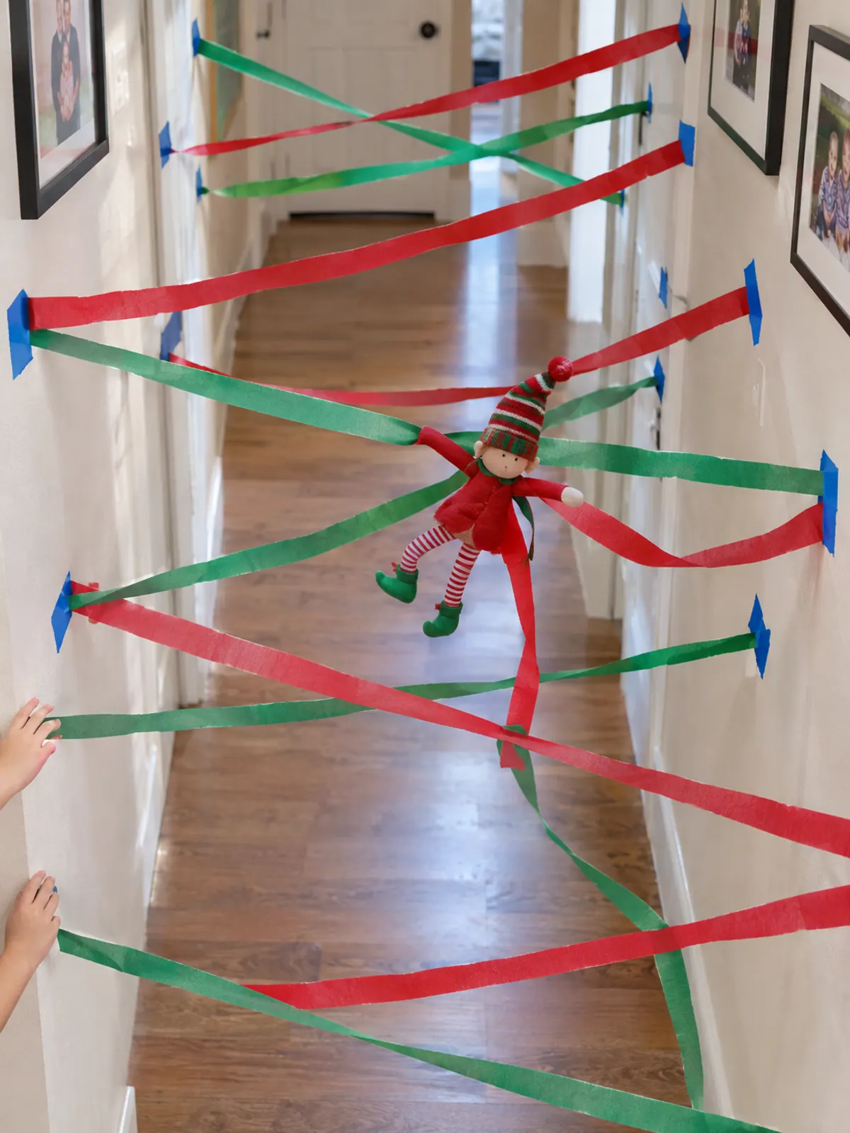 Red and green crepe paper streamers crisscrossed across a home hallway with a felt elf doll tangled in the middle
