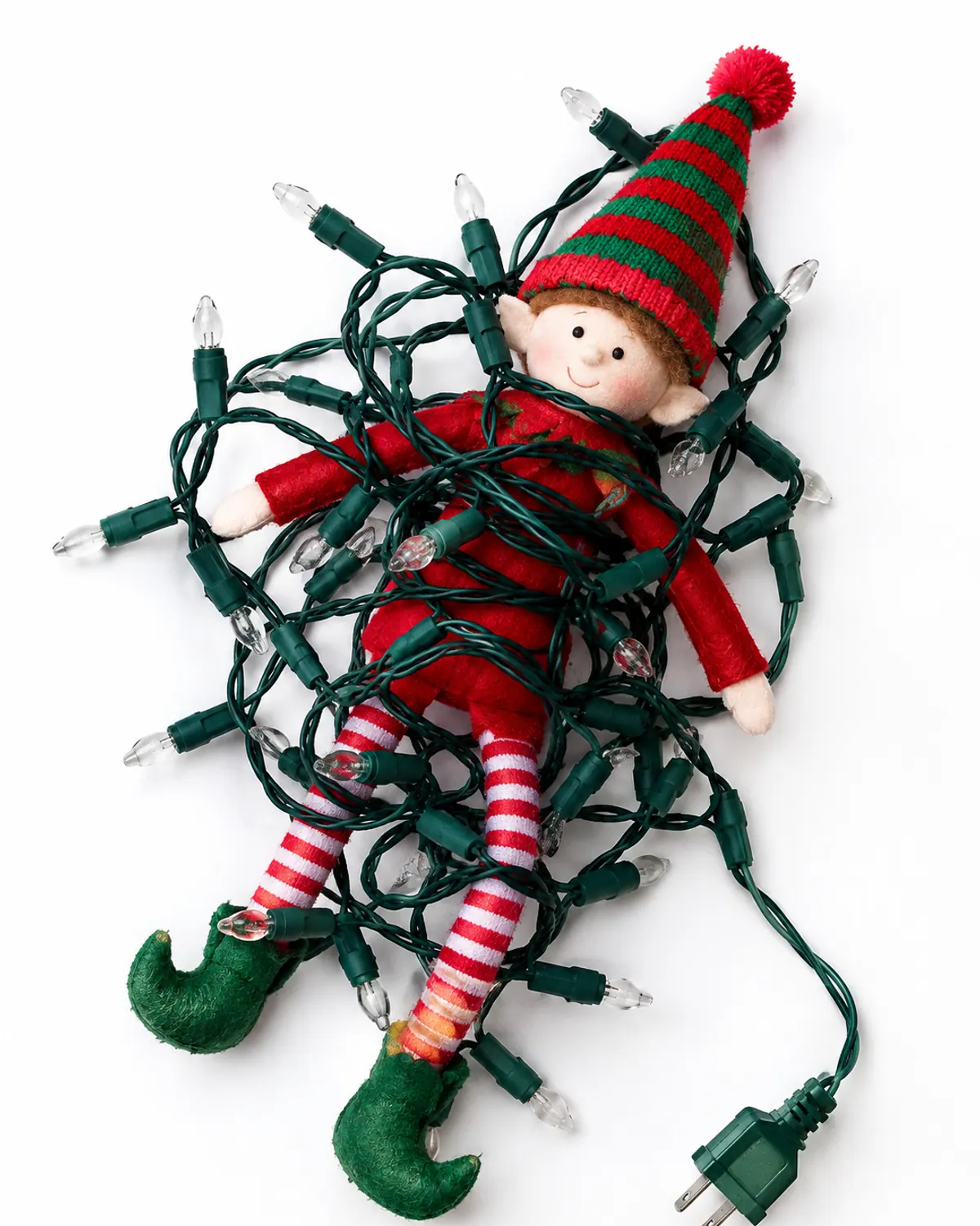 A red felt elf doll on a living room shelf wrapped up in a tangle of unplugged Christmas string lights