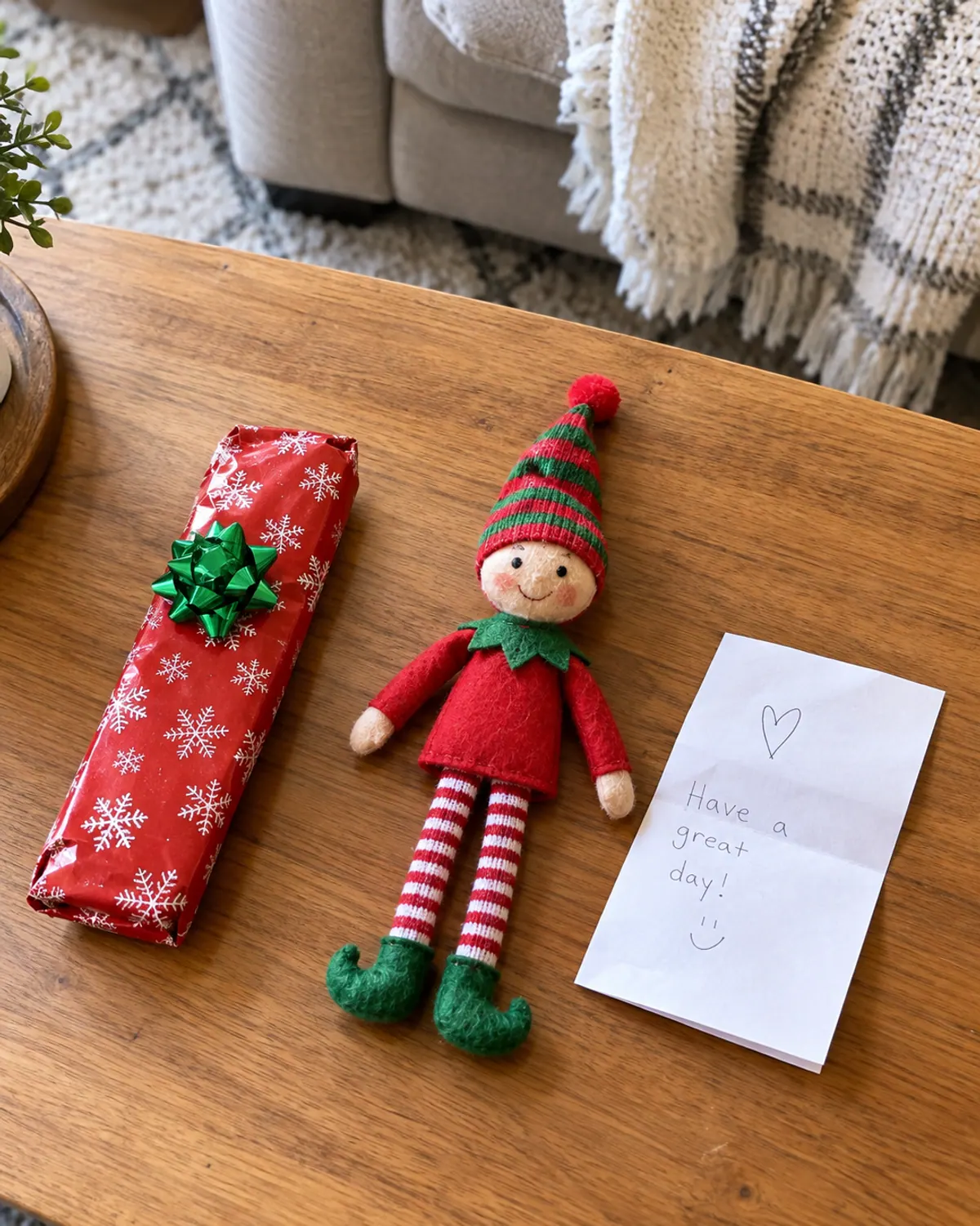 A TV remote wrapped in red wrapping paper with a bow on a coffee table, a felt elf doll sitting beside it with a handwritten note