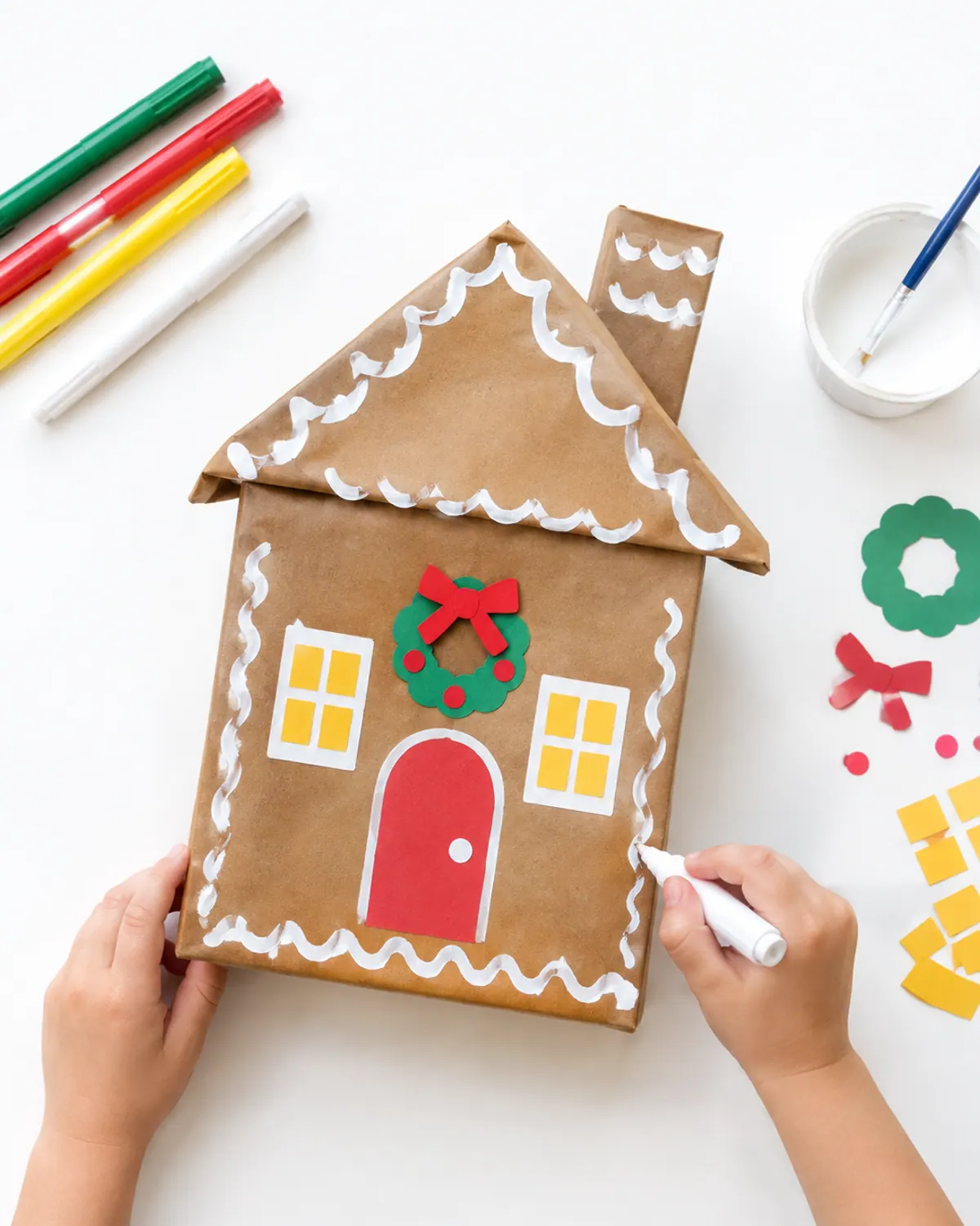 Kids Christmas craft: a cereal box covered in brown paper and decorated as a gingerbread house with white paint icing lines and paper windows