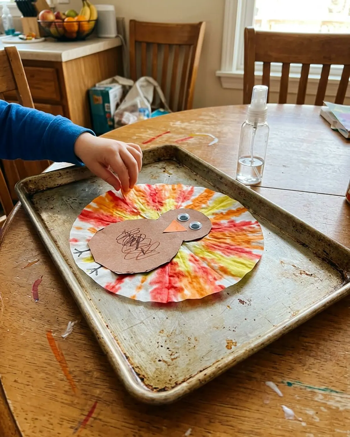 Coffee filter turkey craft with tie-dye orange, red and yellow feathers and a brown paper body drying on a baking sheet